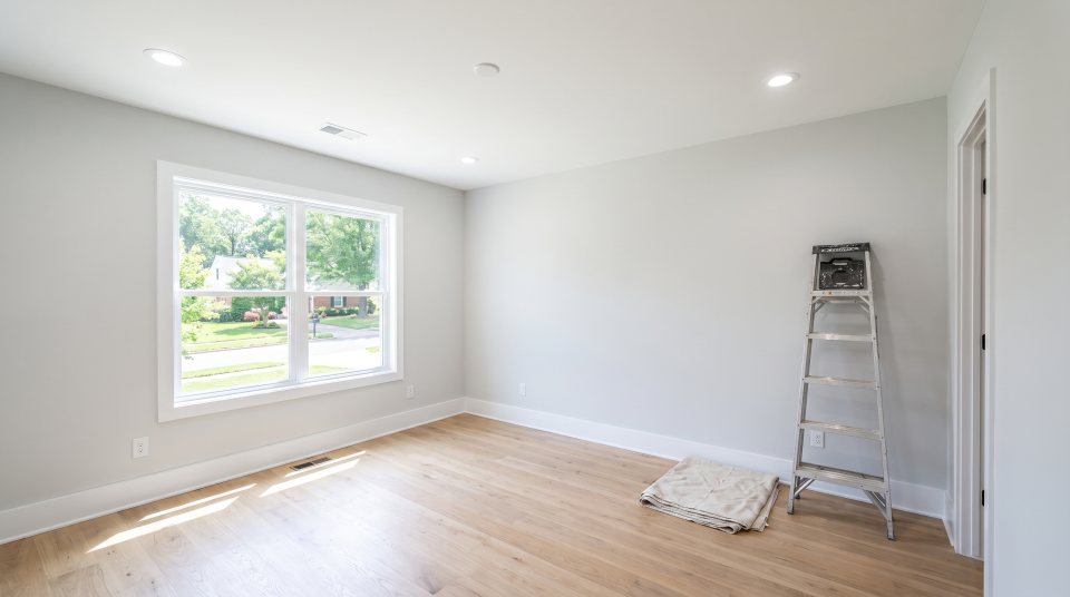 An empty bedroom with a smooth freshly finished white ceiling and recessed lights, a step ladder and a folded drop cloth to one side