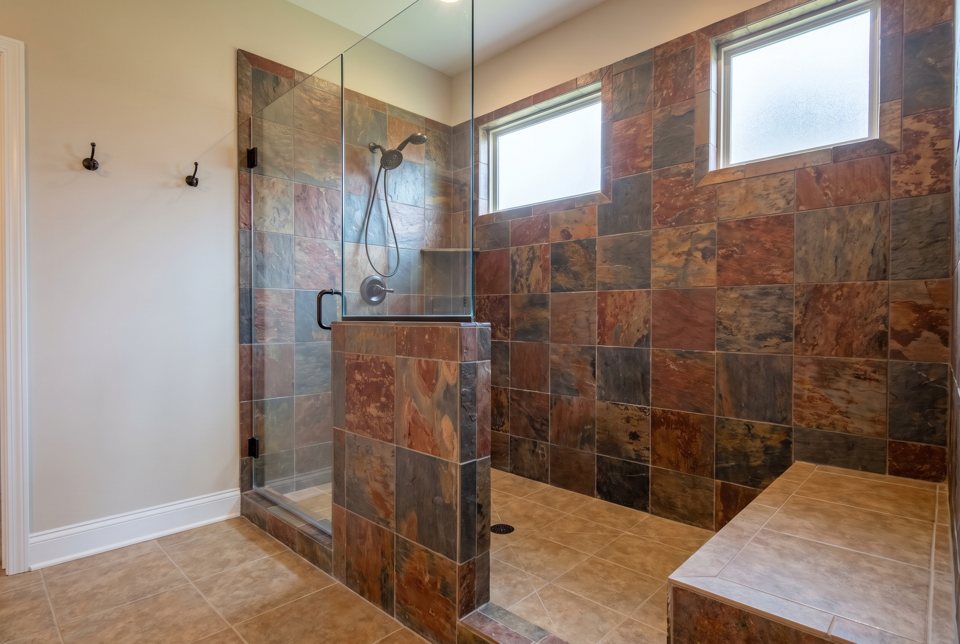 A finished walk-in shower with slate tile walls, a frameless glass door and bronze fixtures