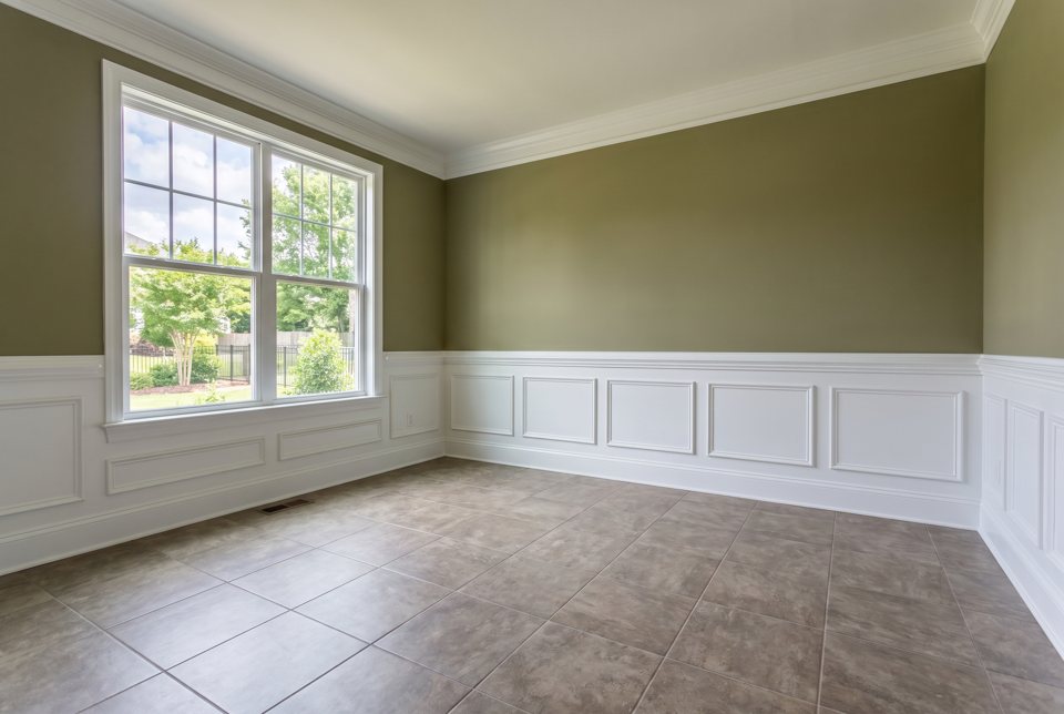 A finished room with sage walls, white wainscot panelling and a tile floor
