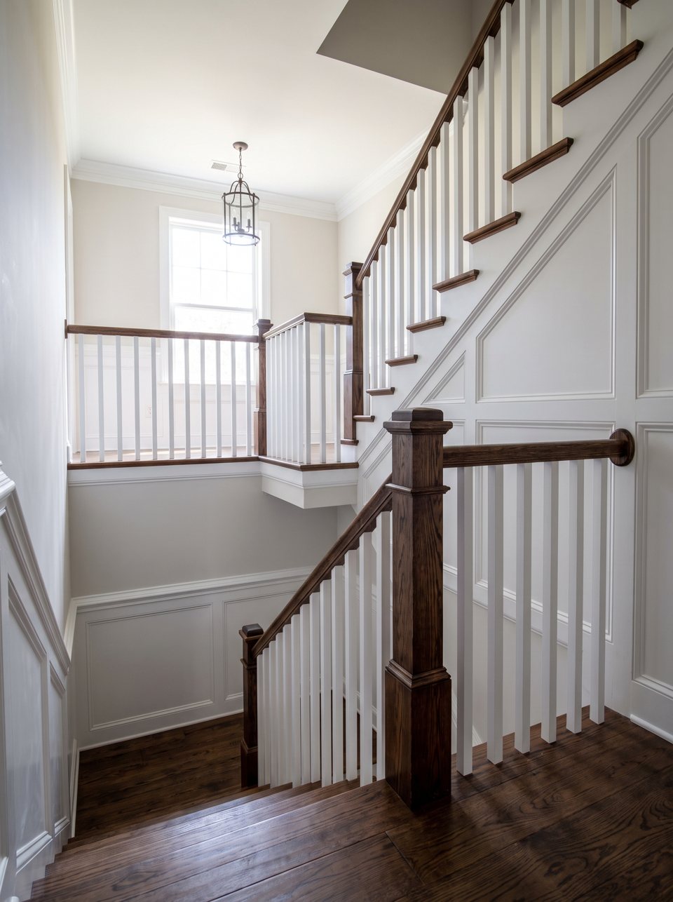 A stair hall with white balusters, a stained handrail and freshly painted walls