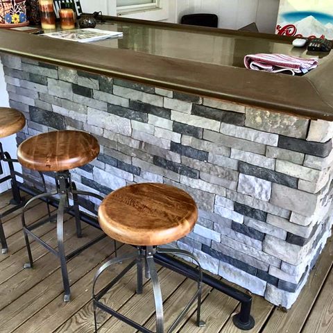 A home bar with a stacked-stone face, a live-edge wooden top and metal stools
