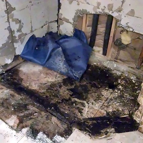 A shower stripped out during demolition, showing water damage beneath the old pan