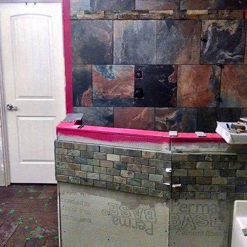 A slate-tiled shower half wall part-way through tiling, with waterproofing membrane still visible above the finished courses