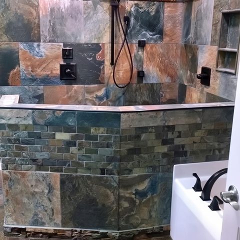 A slate-tiled bathroom with a drop-in tub, bronze fixtures and a tiled surround