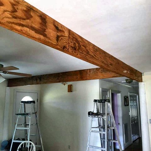 A stained timber beam fixed across a ceiling in a room being repainted