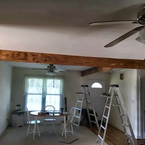 A room with new stained ceiling beams, a ceiling fan and painters' ladders still in place