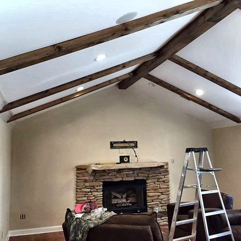 A finished vaulted living room ceiling with dark stained beams above a stacked-stone fireplace