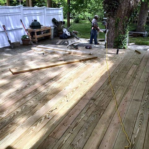 Pressure-treated deck boards being laid on new framing by a member of the crew