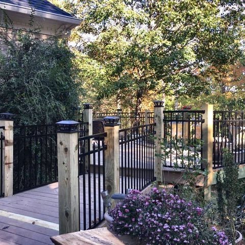 A deck with black aluminum railings, a gate and a matching fence around a planted yard