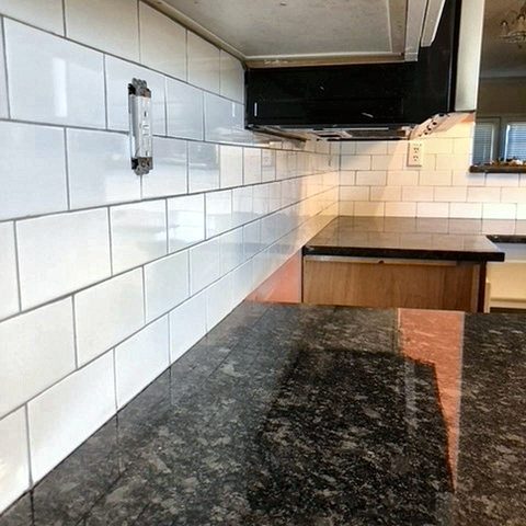 A granite counter meeting a white subway-tile backsplash beneath a range hood