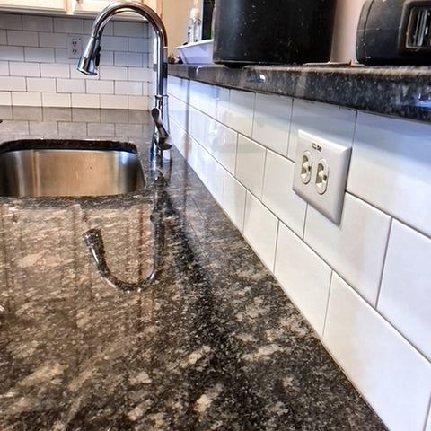 A granite counter with an undermount sink and a white subway-tile backsplash