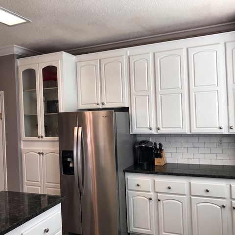 The same style of kitchen after refinishing, with white cabinets and a subway-tile backsplash