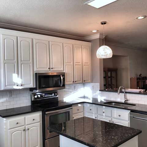 A kitchen with white refinished cabinets, a black granite island and pendant lighting