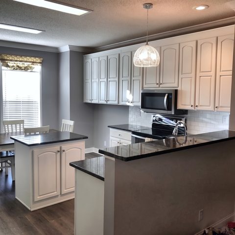 A finished kitchen with white cabinets, a black granite island and a glass pendant light