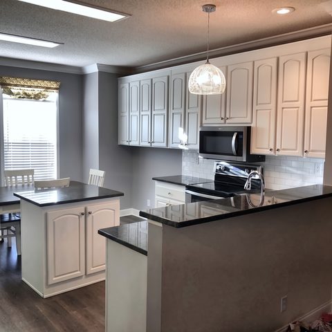 The finished kitchen with white cabinets, black granite counters, a white subway backsplash and pendant lighting