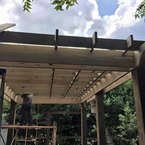 The underside of a finished timber pergola showing rafters and beams against the sky