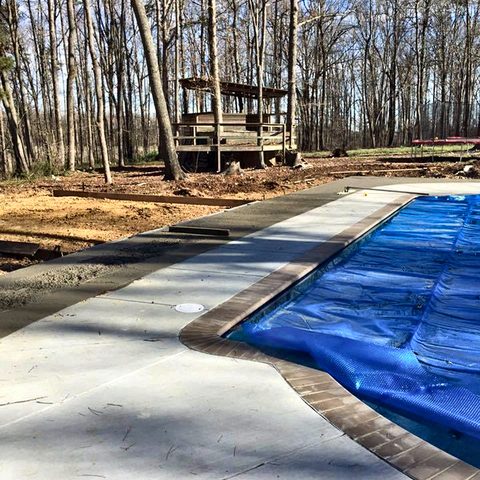 A poured concrete pool deck curing, with the pool covered