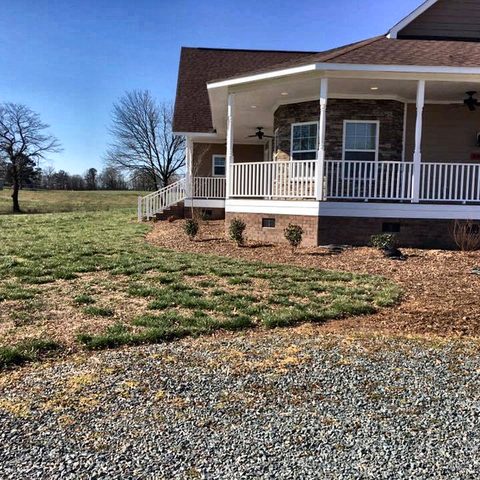 A brick house with a wraparound covered porch seen from across the lawn