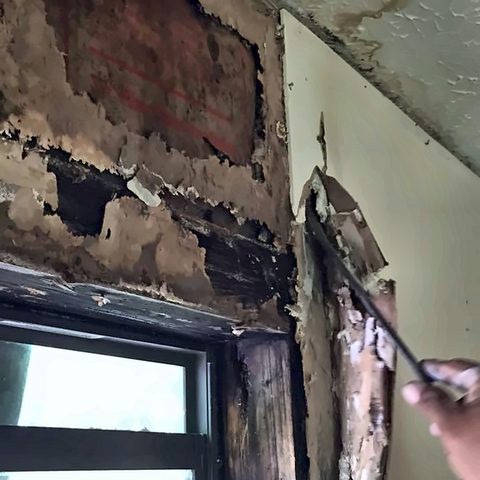 Severe water damage and rot exposed in a wall around a window opening during demolition