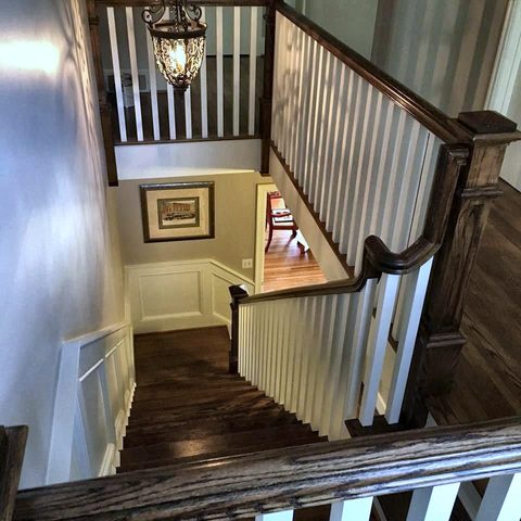 A wide stair hall with a stained rail, white balusters, wainscot and a pendant light
