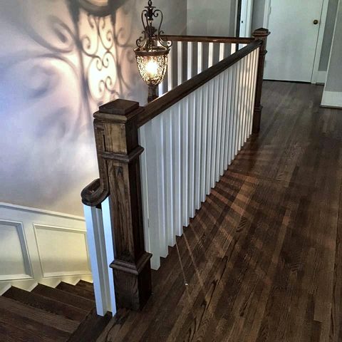 An upper landing with a stained handrail, white balusters and a dark hardwood floor