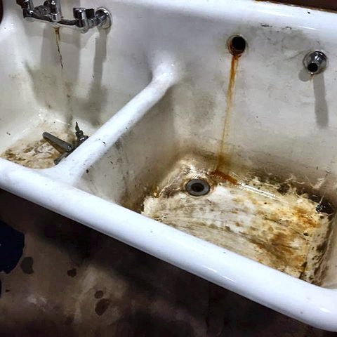 A cast-iron bathtub heavily stained and rusted around the drain before replacement
