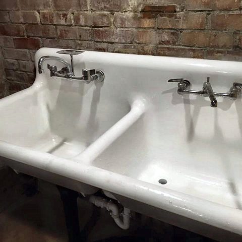 A restored vintage cast-iron double-drainboard utility sink with chrome taps